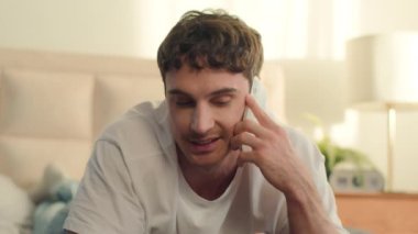 Beyaz Avrupalı bir adam yatak odasında uzanıp cep telefonuyla konuşuyor cep telefonu teknolojisi cihaz. İletişim cihazı. Erkek sohbeti. Arkadaşlık diyaloğu dijital konuşma.