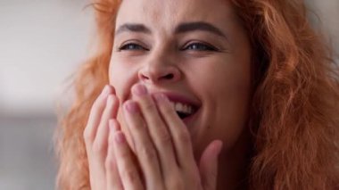 Kafkasyalı kızıl saçlı kadın mutlu bir şekilde eğleniyor, gülüyor, neşe doluyor, elleri kapalı, esprili, komik tepkiler veriyor, kameraya bakıyor, dişlek dişlek, sağlıklı kadın yüzüne gülüyor.