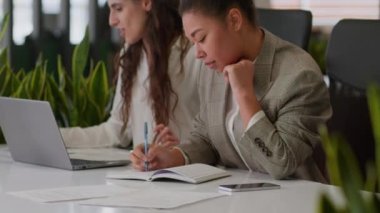 İki çok ırklı kadın iş ortağı kadın Kafkasyalı Afrikalı Amerikalı meslektaşları bayan laptoplar ofis işlerinde birlikte çalışıyorlar iş kadınları belgeleri analiz ediyorlar takım çalışması notları yazıyorlar