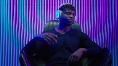 Afrikalı Amerikalı erkek, sandalyede oturmuş kulaklıkla müzik dinliyor. Kablosuz kulaklıkla müzik dinliyor. Sesin tadını çıkarıyor.