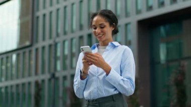 Gülümseyen mutlu Afro-Amerikalı işkadını işveren kadın iş kadını kız bayan yönetici girişimci öğrenci cep telefonu gülümsemesi akıllı telefon uygulaması uygulaması kullanarak şehirdeki internet üzerinden sohbet mesajı