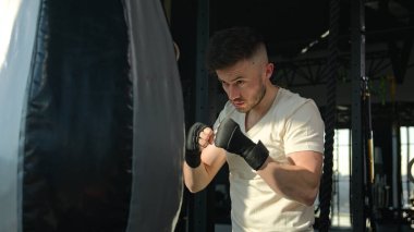 Spor kulübünde kum torbası boks antrenmanı yapan beyaz erkek sporcu boksör sporcu vücut geliştirme sporcusu spor salonunda güçlü vuruş antrenmanları yapıyor.