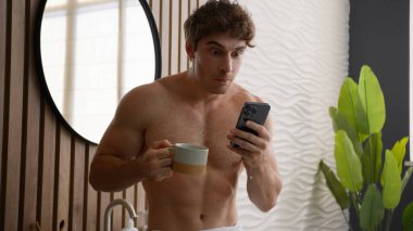 Caucasian naked man looking at mobile phone drinking tea with cup in bathroom shirtless guy morning hygiene check social media read shocked news spitting drink feel shock confused wonder spit coffee clipart