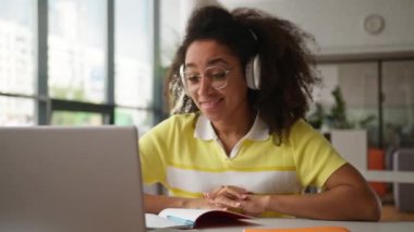 Afro-Amerikalı kız öğrenci kız serbest çalışan Laptop videosu araştırmacısı görev notu yazan kulaklık takarak uzaktaki sanal bilgisayar konferansına konuşan e-öğrenim üniversitesi öğrencisi