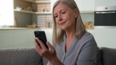 Neşeli, yaşlı, beyaz, yaşlı, olgun bir kadın cep telefonu kullanıyor. Akıllı telefon işkadını, sosyal medya sohbetleri yazıyor. 70 'lerin büyükannesi online oturma odası rezervasyonu yapıyor.