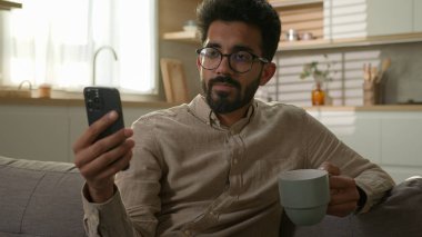 Arap erkek, etnik erkek, rahat koltukta rahat bir şekilde oturup cep telefonu kullanıyor. Mutfakta kahve içiyor. Milenyum bağımsız olarak çalışıyor.