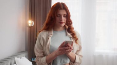 Kafkasyalı mutlu kadın akıllı telefon bulundurduğu için mutlu. Evdeki cep telefonunda e-posta okuyor. Pozitif kız kamera modelinde jest yapıyor. Gülümse. Gözünü kırp.
