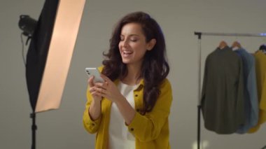 Gülümseyen Kafkasyalı kadın modelin cep telefonuyla müzik açması, akıllı telefon dansı, etrafta oynaşması. Olumlu kadın blogcu hareketini etkileyen vlog yazarı stüdyoda moda şarkısını dinle