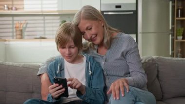 Mutlu yaşlı, olgun, beyaz kadın, son sınıf öğrencisi, yaşlı kadın, büyükanne, gülümseme, torun, çocuk, cep telefonu daktilo oyunu, internet üzerinden malı internette gezdirme, aile evi kanepesi.
