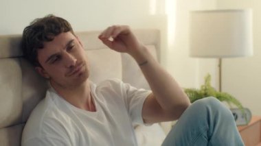 Kafkasyalı genç bir adam yatağında oturup boyun ağrısına dokunuyor. Hasta, bitkin, bitkin, yatak odası ağrısı, rahatsız, mutsuz, mutsuz, üzgün, yüzü tahriş olmuş bir erkek.