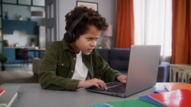 Afro-Amerikalı çocuk kulaklıkla evde bilgisayar yazarak bilgisayar oyunu oynuyor uzaktan oyun oynuyor internet bağımlılığı üzgün mağlubiyet hayal kırıklığını kaybetmiş
