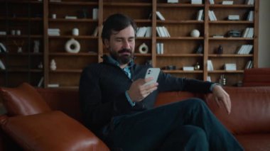 Rahat kahkahalar Kafkasyalı olgun, gülümseyen erkek işadamı müşterisi kullanıcı girişimci cep telefonu tarayıcı akıllı telefon kaydırma sosyal medya uygulaması sosyal medya uygulaması sohbet işi ile dinlenme odası üzerinde çalışıyor.