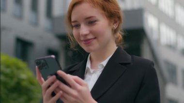 Gülümseyen Kafkasyalı bayan iş kadını, güler yüzlü, güler yüzlü, iş kadını, cep telefonu tutan, sohbet mesajları yazan, şehrin dışındaki sosyal medyada gezinen,