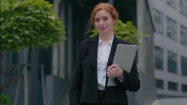 Neşeli beyaz iş kadını kız öğrenci serbest çalışan iş kadını dışarıda kameraya bakarak poz veriyor. Elinde dizüstü bilgisayarla gülümseyen bir işçinin el hareketi onayını göstermesi şehir dışındaki gibi güzel.