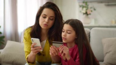 Kafkasyalı düşünceli bir kadın cep telefonu kullanıyor anne alıcı kadın ve küçük kız çocuk ellerinde kredi kartı tutuyor alışveriş parasını ödüyorlar ev içi akıllı telefon sipariş ediyorlar.
