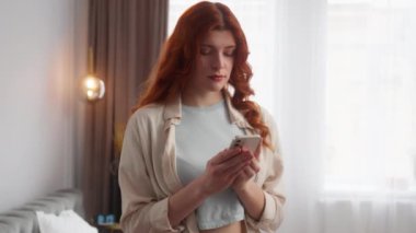 Kafkasyalı kadın cep telefonu kullanıyor. Evde haberleri okuyor. Mutlu kız kameraya bakarken mutlu kadın gülümsemesi bir jest gibi baş parmağını kaldırıyor başarı işareti duygu onayı iyi
