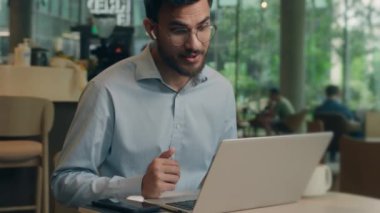 Gülümseyen müşteri turist erkek Hintli Arap iş adamı kulaklıkla iş adamı görüntülü konuşma laptopu konferansı internetteki dost iletişimi kafeterya bilgisayarında uzaktan öğrenim