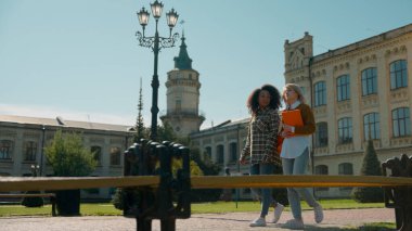 İki öğrenci kız akademinin dışında yürüyor dışarıda çok ırklı kadınlar konuşuyor üniversitede çok ırklı kadınlar koleje gidiyor arkadaş olmak için Afrikalı Amerikalı beyaz bir kızla konuşuyor.