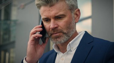 Beyaz, yaşlı, emekli iş adamı olgun, kıdemli işadamı, konuşan, cep telefonu konuşan, cep telefonu takan, telefonu resmi ceket cebine koyan, banka yürüyüp uzaklaşan.