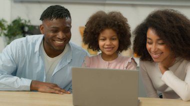Happy smiling family African American parent mother father with little child kid daughter girl talking together greeting hello home kitchen talk video conference call virtual chat with laptop online
