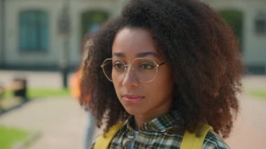 Afro-Amerikan portresi ciddi sakin düşünceli kadın kız yalnız kız üniversite okulunun dışından bakan arkadaşlarıyla konuşan öğrenciler arka plan eğitimi zorbalığı.