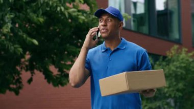 Afro-Amerikan teslimat postacısı üniformalı işçi kurye cep telefonu teslimatçısı erkek sipariş paketi karton paket postacı.