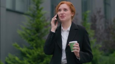Gülümseyen, başarılı, beyaz, iş kadını, bayan, iş kadını, şehirde gezen, arkadaş canlısı, cep telefonlu, akıllı telefon görüşmeleri. Kahve fincanı tutma projesini açık havada tartışın.