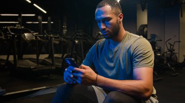 Afrikalı Amerikalı fitness sporcusu spor eğitmeni akıllı telefon sportmenini kullanarak çevrimiçi mesajları tarıyor cep telefonu paylaşımı antreman fotoğrafları sosyal medyada sohbet ediyor spor uygulamasında spor hizmeti veriyor.