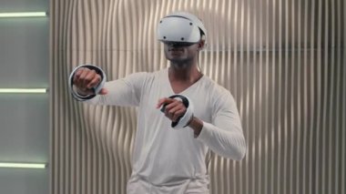 Oyun bağımlısı modern kullanım Afro-Amerikan etnik fütürist erkek oyuncu erkek oyuncu sanal oyun oynuyor VR gözlüklü miğfer takıyor video oyunu fütürizm siber uzay metaevreleri oynuyor.