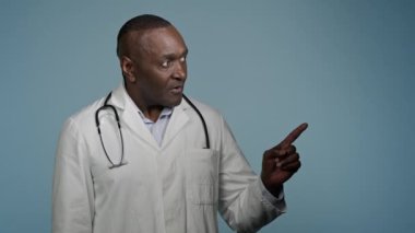 Afro-Amerikalı erkek doktor erkek doktor. Tıp hizmetleri için sağlık hizmeti promosyonu profesyonel tedavi için mavi stüdyo şablonunda duran metni yazmak için boş bir yeri işaret ediyor.