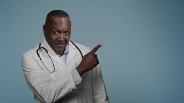 Gülümseyen Afro-Amerikalı doktor doktor, stüdyo mavi arka planda, tıp hizmetlerinin reklamını yapmak için mesaj şablonu yazmak için boş bir yeri işaret ediyor.