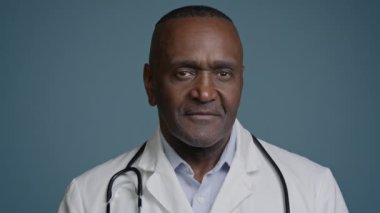 Portre erkek özgüveni olan başarılı Afro-Amerikan Etnik doktor, profesyonel sağlık çalışanı. Stüdyo mavi arka plan hastane klinik hizmetlerinde gülümseyen kameraya bakıyor.