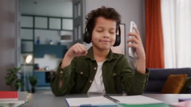 Komik Afrika kökenli Amerikalı oğlan çocuk öğrenci öğrenim öğrenim görüyor ara vermeyi kulaklıkla müzik dinlemeyi müzik dinlemeyi müzik dinlemeyi dans etmeyi telefon tutmanın keyfini çıkar.