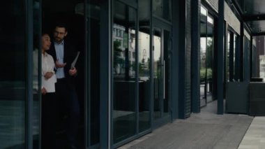 Konuşan iki çok ırklı iş arkadaşı şehir dışında ofisten ayrılırken Afrika kökenli Amerikalı kadın iş kadını, beyaz erkek işadamı, erkek, dizüstü bilgisayar klasörü.