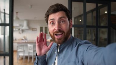 Gülümseyen Kafkasyalı yetişkin blogcu elinde cep telefonu kamerası, pozitif erkek baba konuşuyor video blogunda babamın evde çevrimiçi yayın yapan film odası turuna el sallamasına seviniyor.