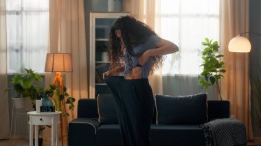 Mutlu, şaşkın, gülümseyen, etnik İspanyol kadın, yaşlı kot pantolon giyen, zayıf kadın, kilo kaybı, spor, beslenme, sağlıklı bir oturma odası.