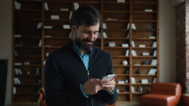 Gülen Kafkasyalı olgun yönetici erkek iş adamı patron cep telefonu sohbet uygulaması cep telefonu oyunu oynayarak, sosyal medyada gezinerek ev içi sipariş vererek eğleniyor.