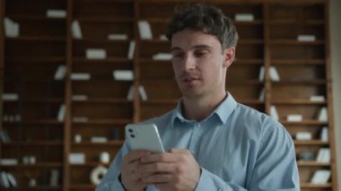 Gülen gen z mutlu Kafkas iş adamı Avrupalı erkek geniş gülümsemeli iş adamı rahat patron cep telefonu mesajlaşması kullanıyor daire içi internet mesajları gönderiyor