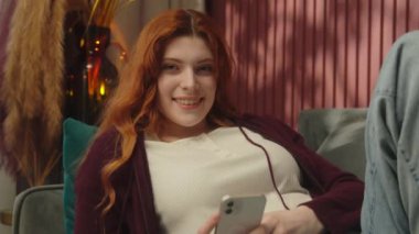 Gülümseyen kadın ev sahibi beyaz kadın kiracı daire kanepesinde uzanan mutlu kızıl saçlı bağımlı cep telefonu internet üzerinden alışveriş siparişi dağıtımı. Evde rahatla.