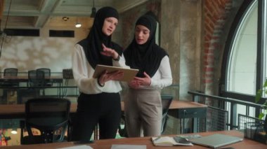 İki iş kadını Arap Müslüman kızlar çok ırklı iş kadınları tesettürlü kadın takım tasarımcısı kadın tasarımcılar iş arkadaşları planlama ofisi projesini tartıştılar dijital tablet ortaklığı kurdular