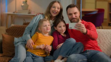 Küçük ebeveynler mutlu Kafkasyalı aile blogcuları fotoğraf cep telefonu kameraları, gülücükler, selfie komik yüzler, kızlar, anneler, babalar akşam evde video blogu kaydediyor.