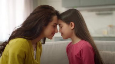Sevimli bir aşk anı, aile bağı, beyaz kadın anne, alnına dokunuyor, anaokulundaki küçük kız çocuğuna sarılıyor, kanepeye sarılıyor, evde rahat bir evde anneliği kucaklıyor.