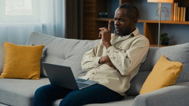 Düşünceli, şaşkın, afro-amerikan, iş adamı iş adamı, ev koltuğunda dizüstü bilgisayarla çalışan, iş problemini çözen, ciddi, düşünceli, yeni fikirler arayan, düşünceli bir erkek.