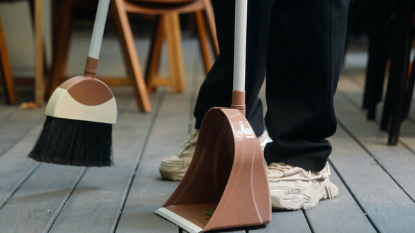 Indian Arabian man cafe worker in apron entrepreneur male businessman guy waiter cleaner working small business owner sweeping leaves using broom cleaning preparing restaurant for visitors city street