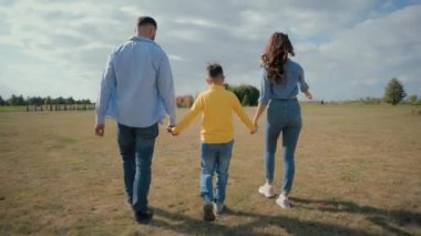 Kafkasyalı aile gezintisi, park alanını araştırmaktan bahsediyor. Anne kadın el ele tutuşuyor baba erkek el ele tutuşuyor küçük çocuk çocuk doğayı gösteriyor parmakla işaret ediyor dışarıda yürüyor