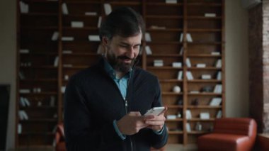 Gülen Kafkasyalı olgun yönetici erkek iş adamı patron cep telefonu sohbet uygulaması cep telefonu oyunu oynayarak, sosyal medyada gezinerek ev içi sipariş vererek eğleniyor.