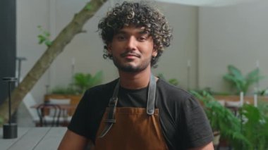 Neşeli Latin Amerikalı etnik erkek, gülümseyen kafe çalışanı, önlüklü garson, garson, barista, küçük işletme sahibi, kasabanın dışında gülümseyen kameraya bakıyor. İstihdam sokak yemekleri