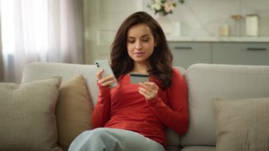 Gülümseyen Kafkasyalı kadın mutlu müşteri alıcı kız iş kadını cep telefonu kullanıyor kredi kartı kullanıyor online ödeme bankacılığı ecommerce ev kanepede internet alışverişi satın alıyor