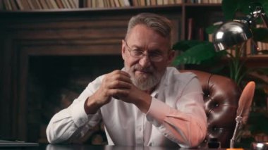 Kendinden emin, yaşlı, beyaz, olgun bir erkek kamera önünde el ele tutuşmuş ofis işadamı yakışıklı, yaşlı çalışan portresi liderinin içindeki iş adamına bakıyor.