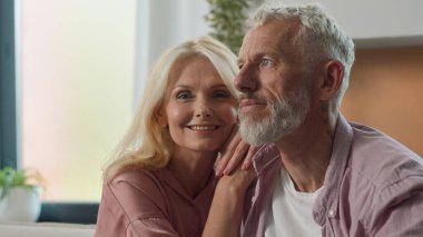 Mutlu bir gülümseme beyaz bir çift evli aşık bir adam koca sarılmış oturma odasında birbirine sarılıyor olgun ev sahipleri arasında bağ kuruyor hayallerinin tadını çıkarıyorlar.